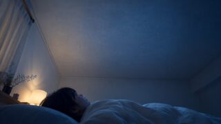 布団の中で天井を見上げる女性、夜の静謐